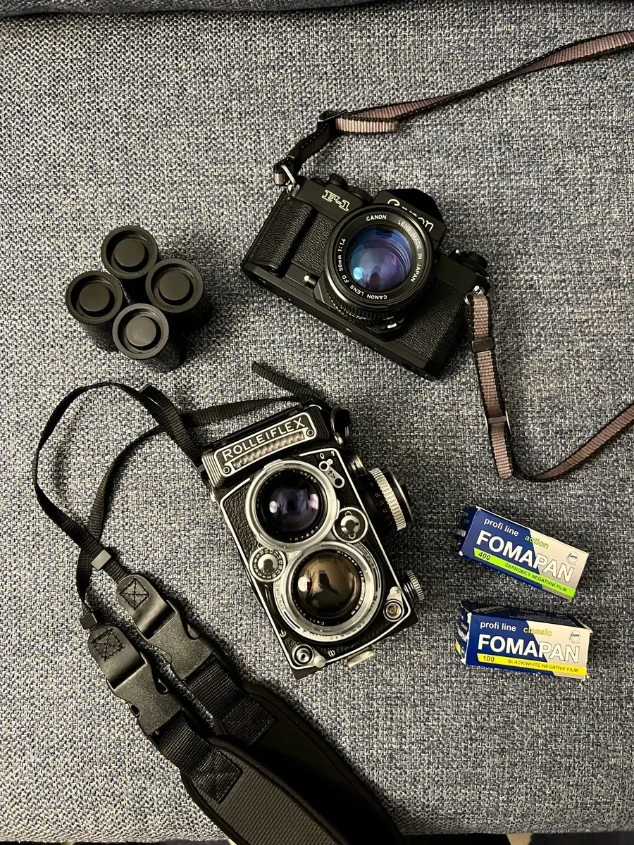 Overhead view of two film cameras on fabric — an SLR and the Rolleiflex 2.8F — with spent rolls and boxes of Fomapan.