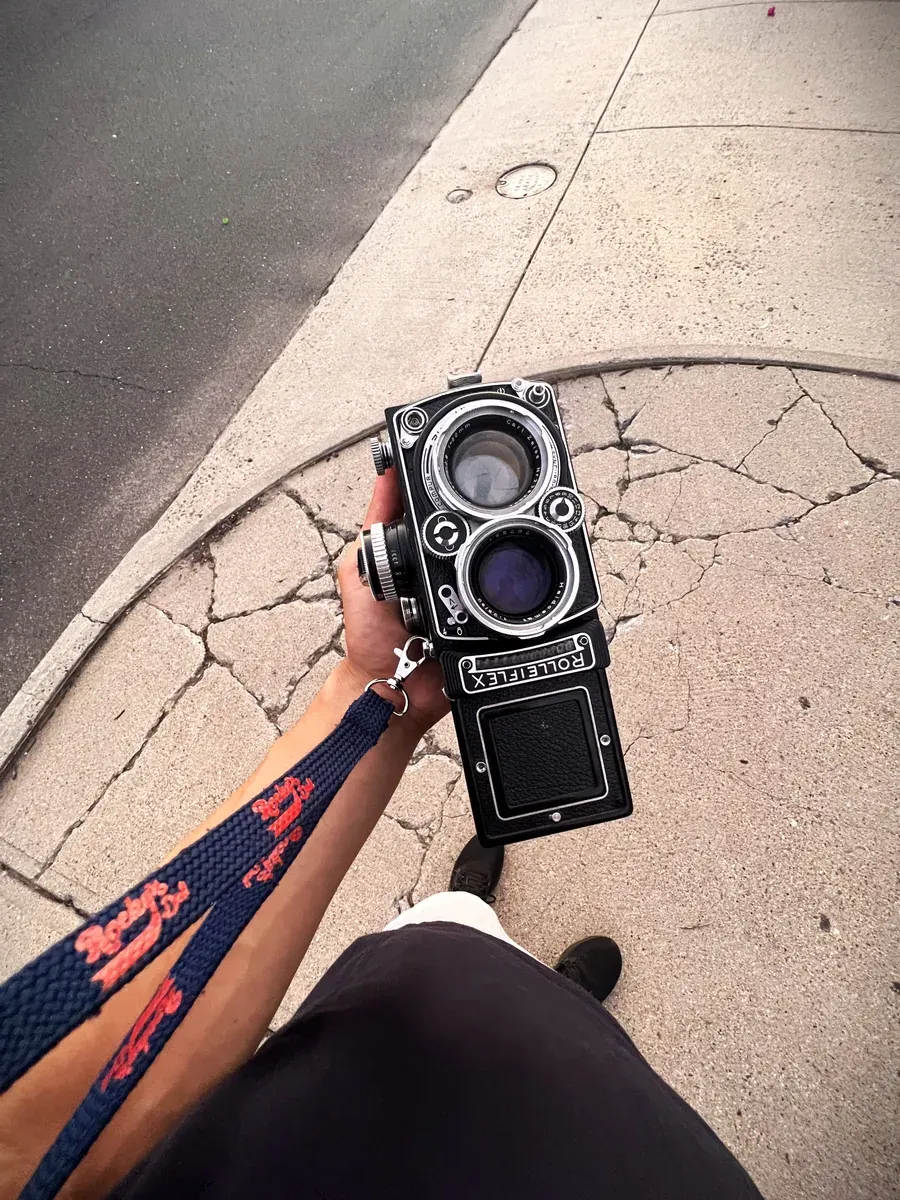 Looking down at the Rolleiflex 2.8F held at the photographer's side on a cracked sidewalk.