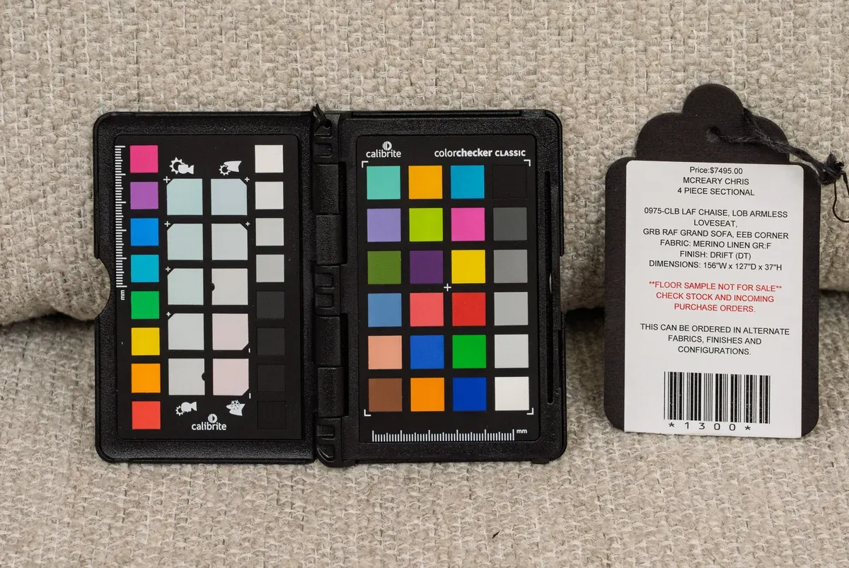 An open Calibrite ColorChecker Classic, its color and gray patches in rows, lying on an oatmeal linen sectional beside the sofa's floor-sample tag.
