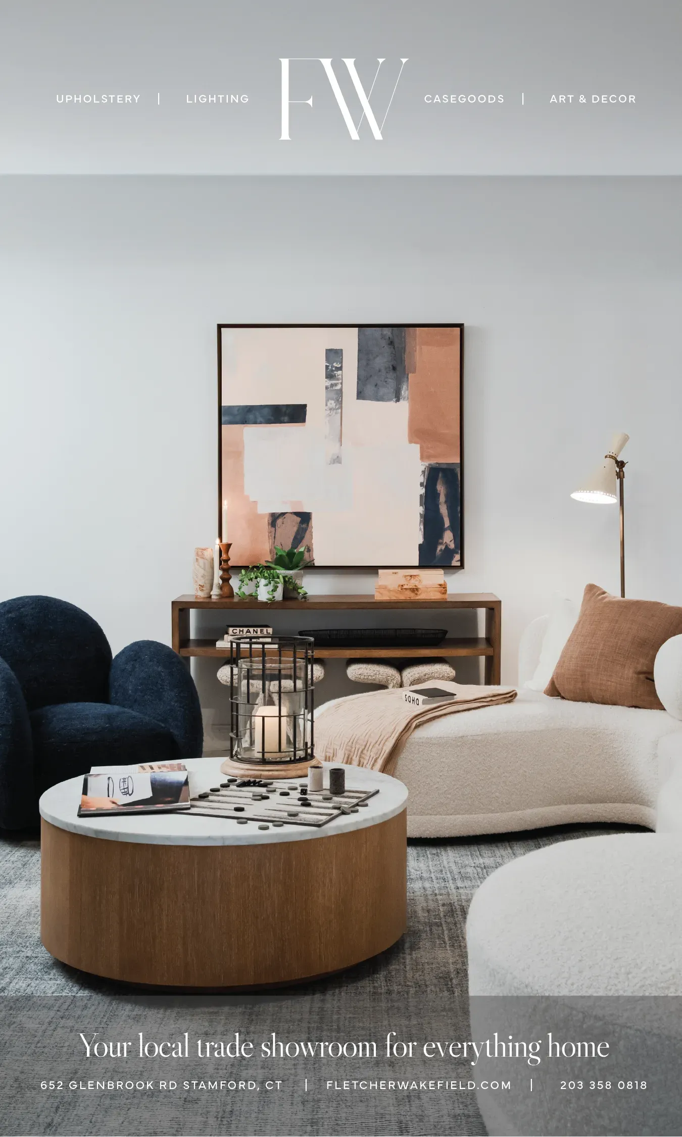 Fletcher Wakefield's ad: a navy bouclé armchair and a white curved sofa around a round oak and marble coffee table set with a backgammon board, below an abstract painting in blush and navy over a walnut console, under the FW mark and the line 'Your local trade showroom for everything home'.