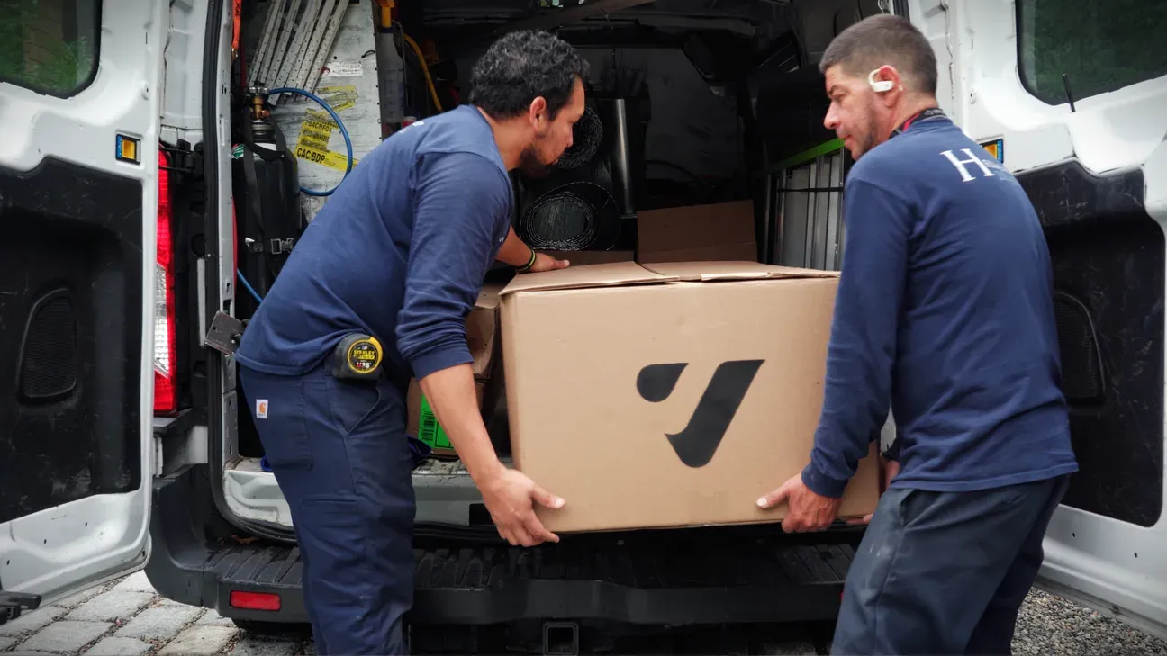 Two technicians in Vibrant work shirts unloading a branded cardboard box from a service van during a field install