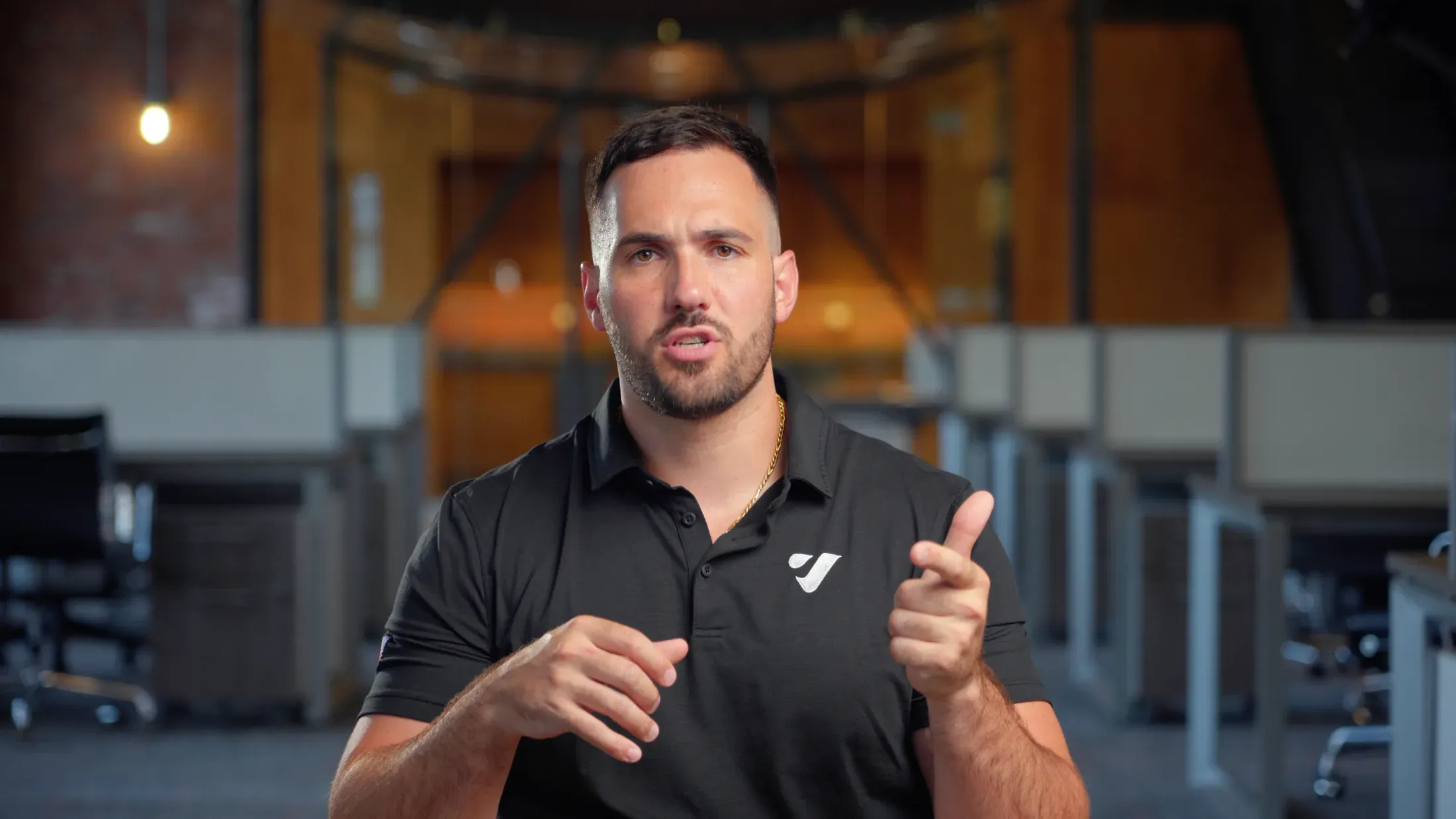 A man in a black Vibrant polo speaking to camera in an open-plan office with brick walls and exposed ductwork, a still from the StartEngine film.